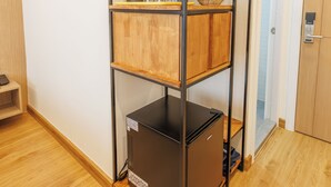 A compact room with a built-in shelving unit, a compact refrigerator, and a wooden floor. - Believe Inn (Bangkok)