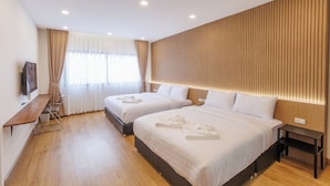 A modern hotel room with two beds, a wooden floor, a TV on the left, and a wooden headboard. - Believe Inn (Bangkok)
