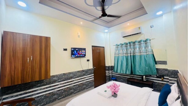 A hotel room with a bed, a wooden wardrobe, a television, and a ceiling fan. - Gitanshi Palace (Ayodhya)