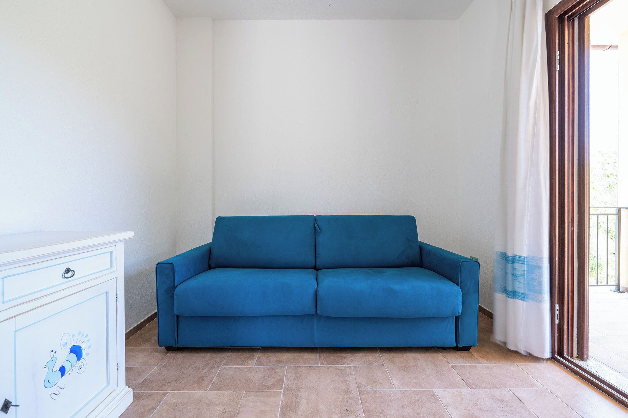 A blue sofa in a room with a white cabinet and a sliding glass door.