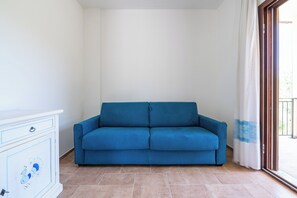 A blue sofa in a room with a white cabinet and a sliding glass door. - AffittaSardegna - Trilo Euforbia  (Siniscola)