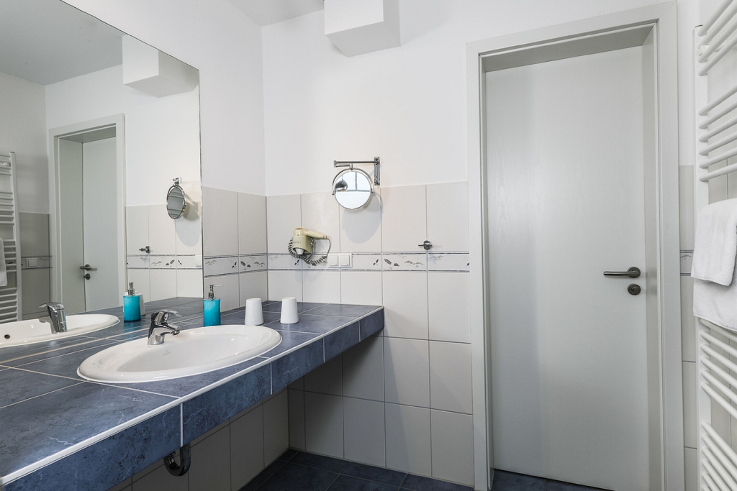 Une salle de bain avec un grand miroir, deux lavabos, un porte-serviettes et des toilettes.