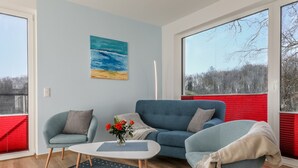 Un salon moderne avec un canapé bleu, deux fauteuils, une table basse et un tableau représentant une scène de plage.