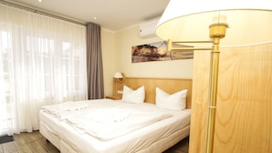 A hotel room with a large bed, a bedside lamp, a painting on the wall, and a window with curtains. - Rügen vacation near the beach - Bungalow Hanseatchen (Baabe)