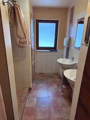 Un baño pequeño con dos lavamanos, una ventana y una toalla colgada de un gancho.