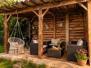 Una cabaña de madera con porche cubierto, muebles de mimbre y plantas colgantes.