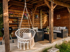 Una cabaña de madera con un sillón colgante, muebles de mimbre y una parrilla.
