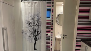 A bedroom with a bed, a wardrobe, a bathroom with a sink and mirror, and a shower curtain with a tree design. - Accommodation in Tibro with free WiFi and parking. (Tibro)