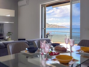 A dining area with a table set for two, a sofa, and a view of the sea through large windows. - Look Of Passion (Giardini Naxos)