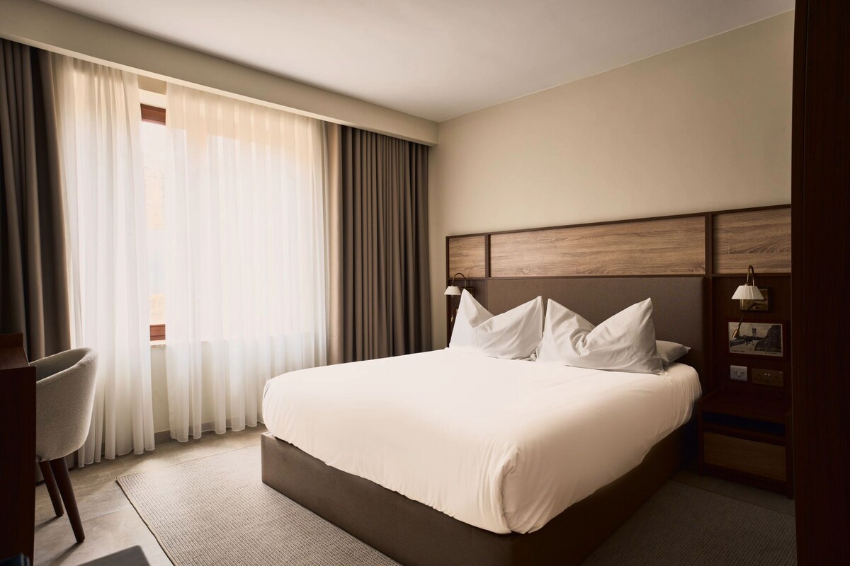 A hotel room with a large bed, a desk, and a chair.