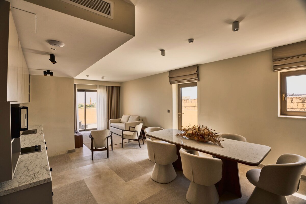 A modern hotel room with a dining area, a sofa, and a view of the outdoors.