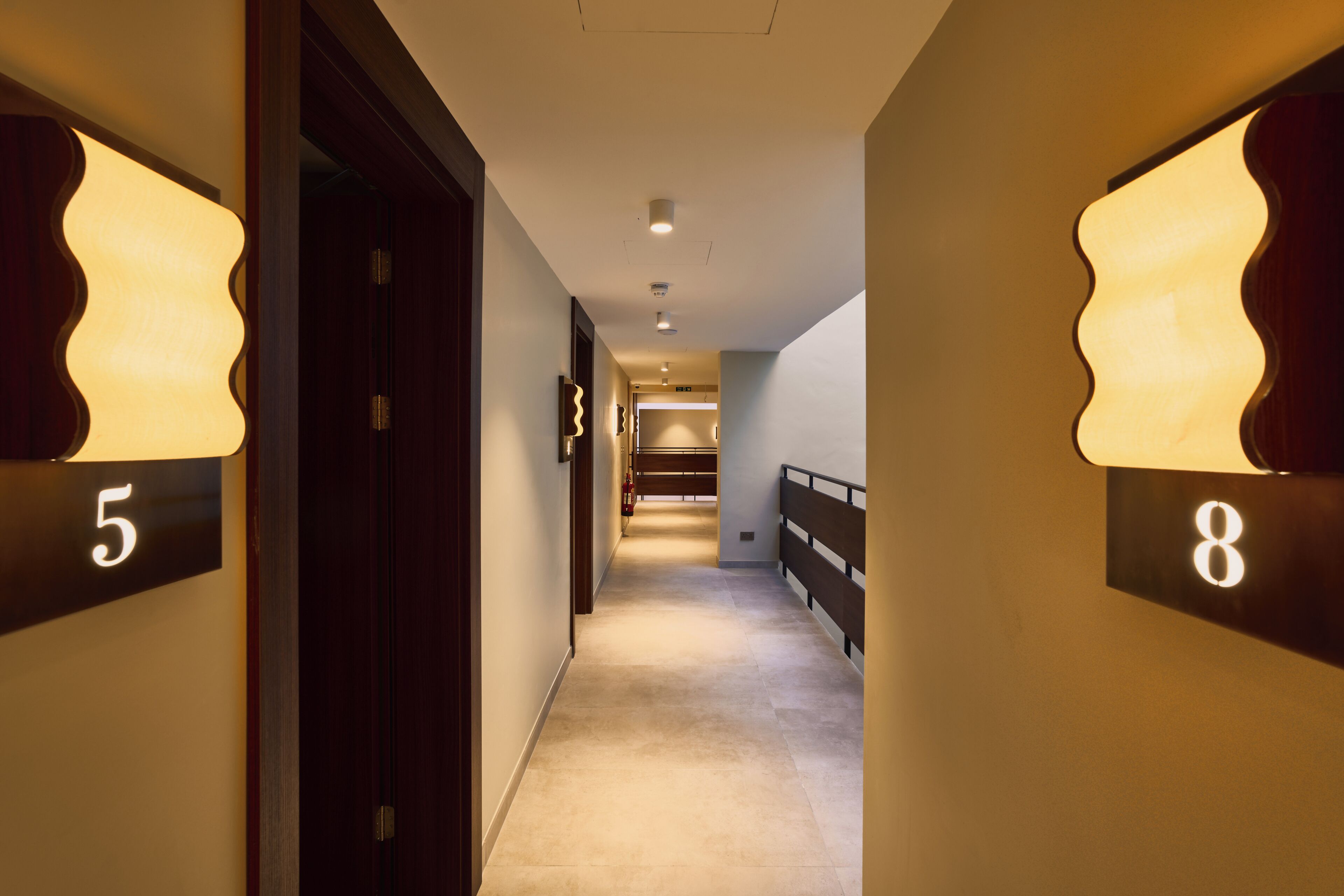 A hotel hallway with doors numbered 5 and 8, a carpeted floor, and a railing on the right.