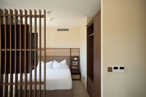 A hotel room with a bed, a nightstand, a lamp, a wardrobe, and a wall-mounted thermostat.