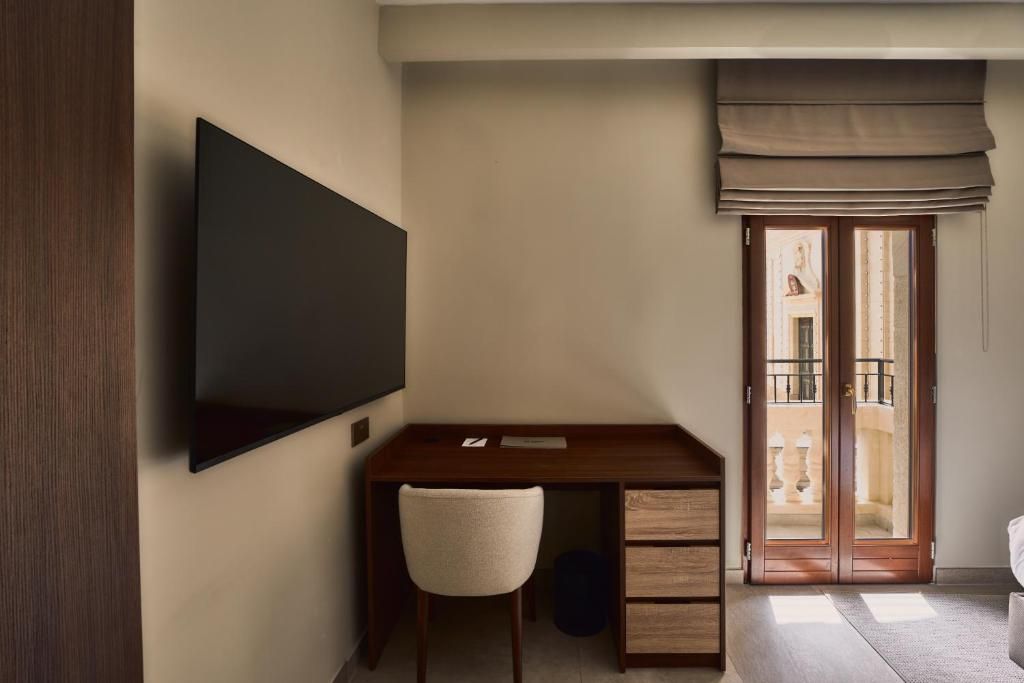 Une chambre dotée d’un téléviseur à écran plat fixé au mur, d’un bureau en bois avec une chaise, d’une porte-fenêtre coulissante donnant sur un espace extérieur et d’une petite poubelle.