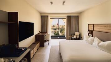 A hotel room with a bed, a desk, a TV, a balcony with a view, and a window with curtains.