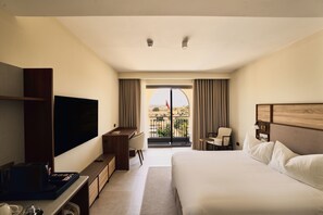 A hotel room with a bed, a desk, a TV, a balcony with a view, and a window with curtains. - Quaint Signature Hotel San Lawrenz (San Lawrenz)
