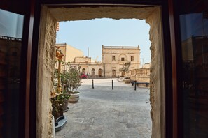 Une cour avec un chemin en pierre, des plantes en pot et un bâtiment aux arches en arrière-plan.