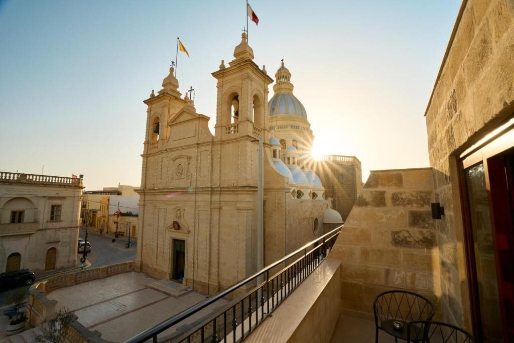 A historic building with a bell tower and dome, a balcony with a railing, and a clear sky.