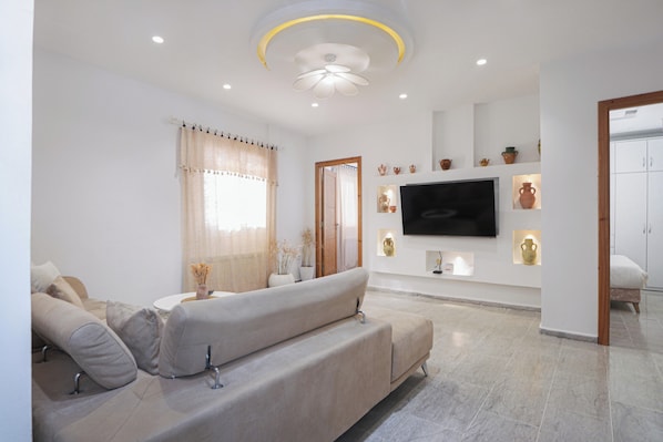 A modern living room with a sofa, television, and decorative items on the wall. - Charming Apartment in Historic Carthage With Modern Comforts (Sidi Bou Said)