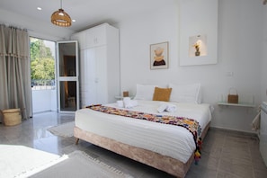 A bedroom with a large bed, a wardrobe, a bedside table with a lamp, and a view through an open door. - Charming Apartment in Historic Carthage With Modern Comforts (Sidi Bou Said)