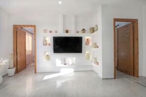 A spacious room with a flat-screen TV mounted on the wall, wooden doors, and a potted plant.