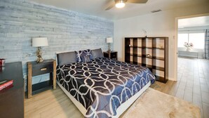 Een slaapkamer met een bed, twee nachtkastjes, een plafondventilator, een boekenplank en uitzicht op buiten.
