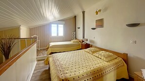 Ein Schlafzimmer mit zwei Betten, Holzbalkendecke, einem Fenster und einer kleinen Wandleuchte.