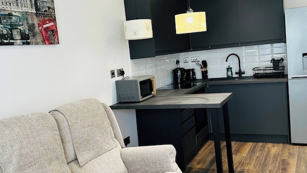 Une cuisine moderne avec des meubles de couleur sombre, un four à micro-ondes et un évier. Le salon comprend un canapé et une table à manger.