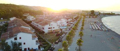 Un pueblo costero con playa, edificios blancos y coches aparcados a lo largo del paseo marítimo.
