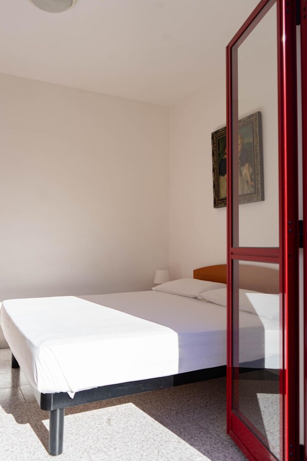 Un lit simple avec un matelas blanc et une tête de lit en bois, dans une pièce aux murs blancs.