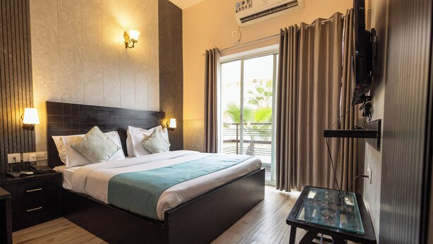 Una camera d'albergo con un letto grande, un tavolino, una TV e un balcone con tende.