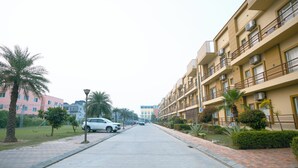 Una strada residenziale con marciapiede lastricato, auto parcheggiate e edifici a più piani con balconi e condizionatori.