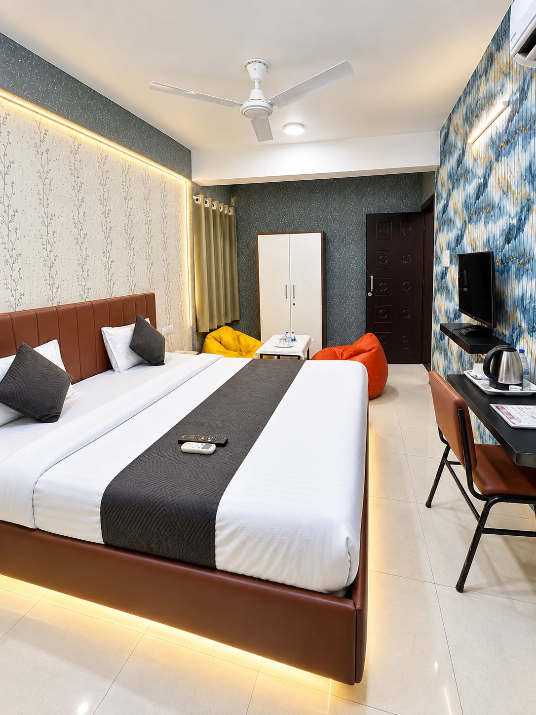 Quarto de hotel moderno com uma cama grande, uma escrivaninha com cadeira, um guarda-roupa e uma televisão.