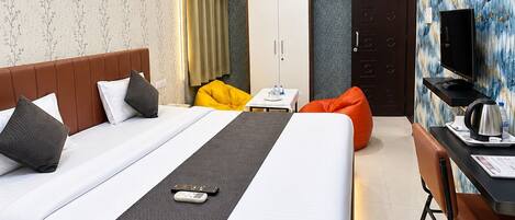 Quarto de hotel moderno com uma cama grande, uma escrivaninha com cadeira, um guarda-roupa e uma televisão.
