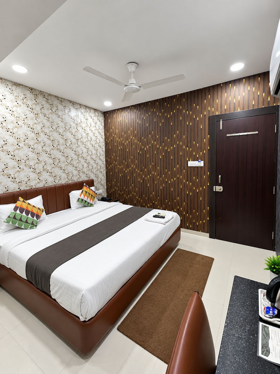Ein modernes Hotelzimmer mit einem großen Bett, einem Deckenventilator, einer Wand mit Holzapplikationen und einer Tür.