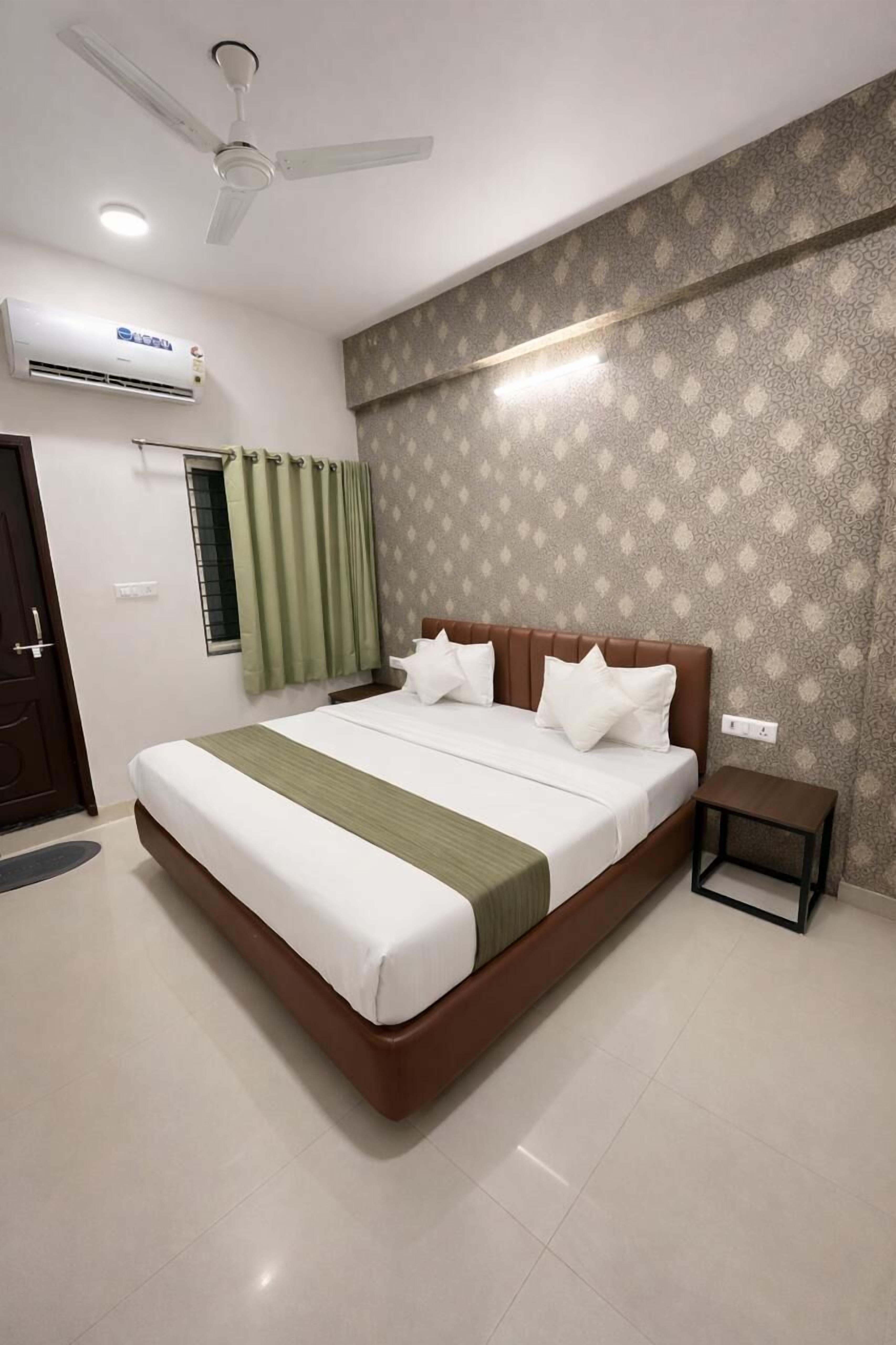 A hotel room with a large bed, a ceiling fan, an air conditioning unit, a small bedside table, and a patterned wall.
