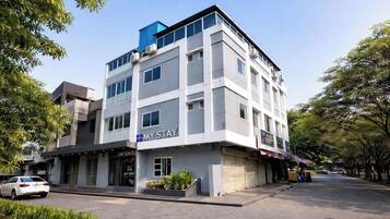 Un hotel de varios pisos con un letrero llamativo que dice 'MY STAY', una fachada plana y un estacionamiento con un auto blanco.