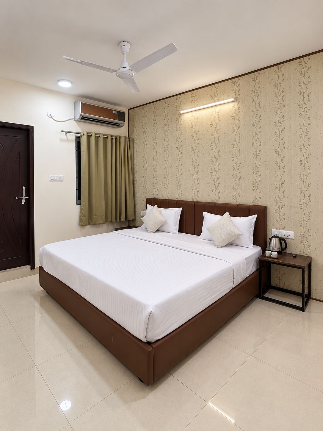 A hotel room with a bed, a nightstand, a ceiling fan, an air conditioning unit, and a door.