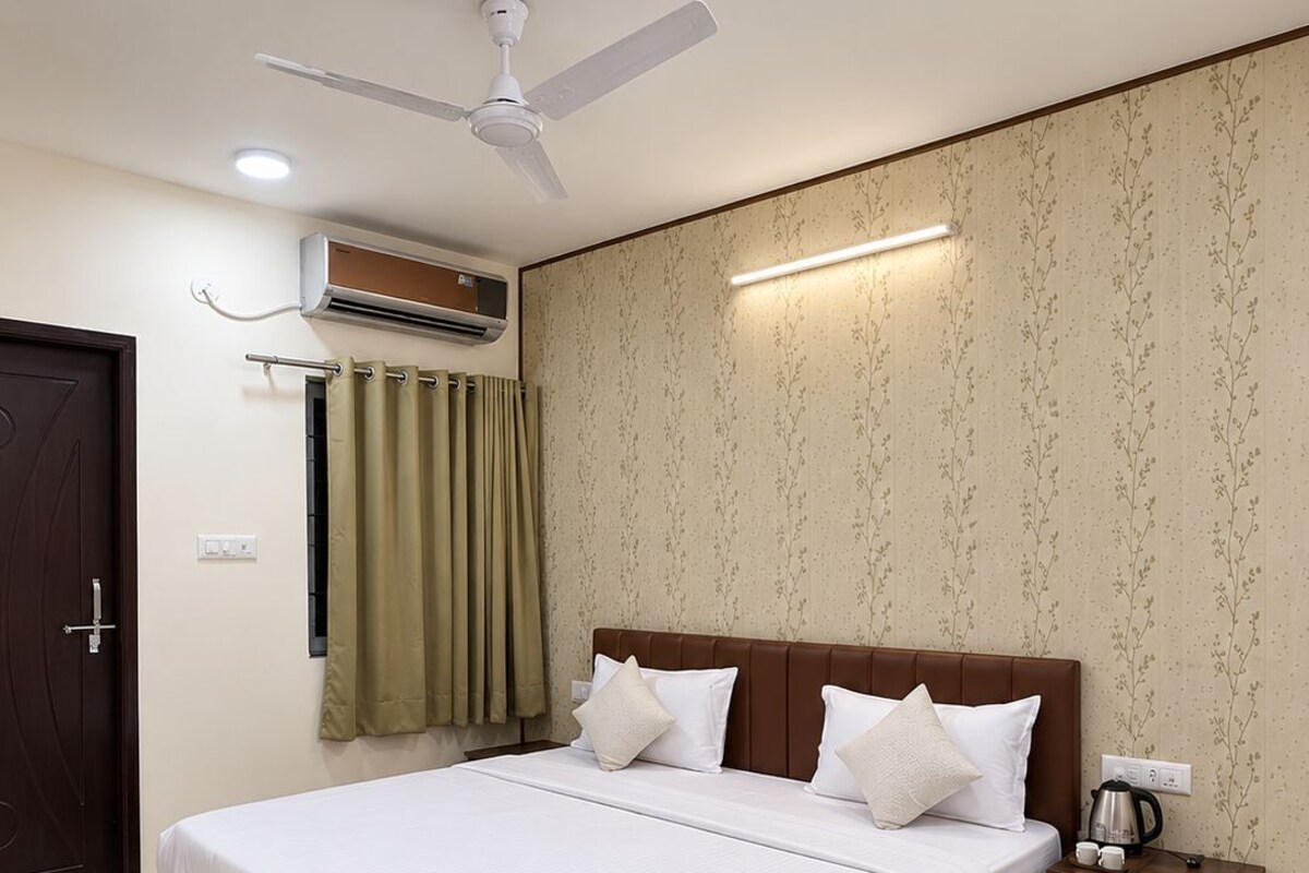 Une chambre d’hôtel avec un lit, une table de chevet, un ventilateur de plafond, un appareil de climatisation et une porte.