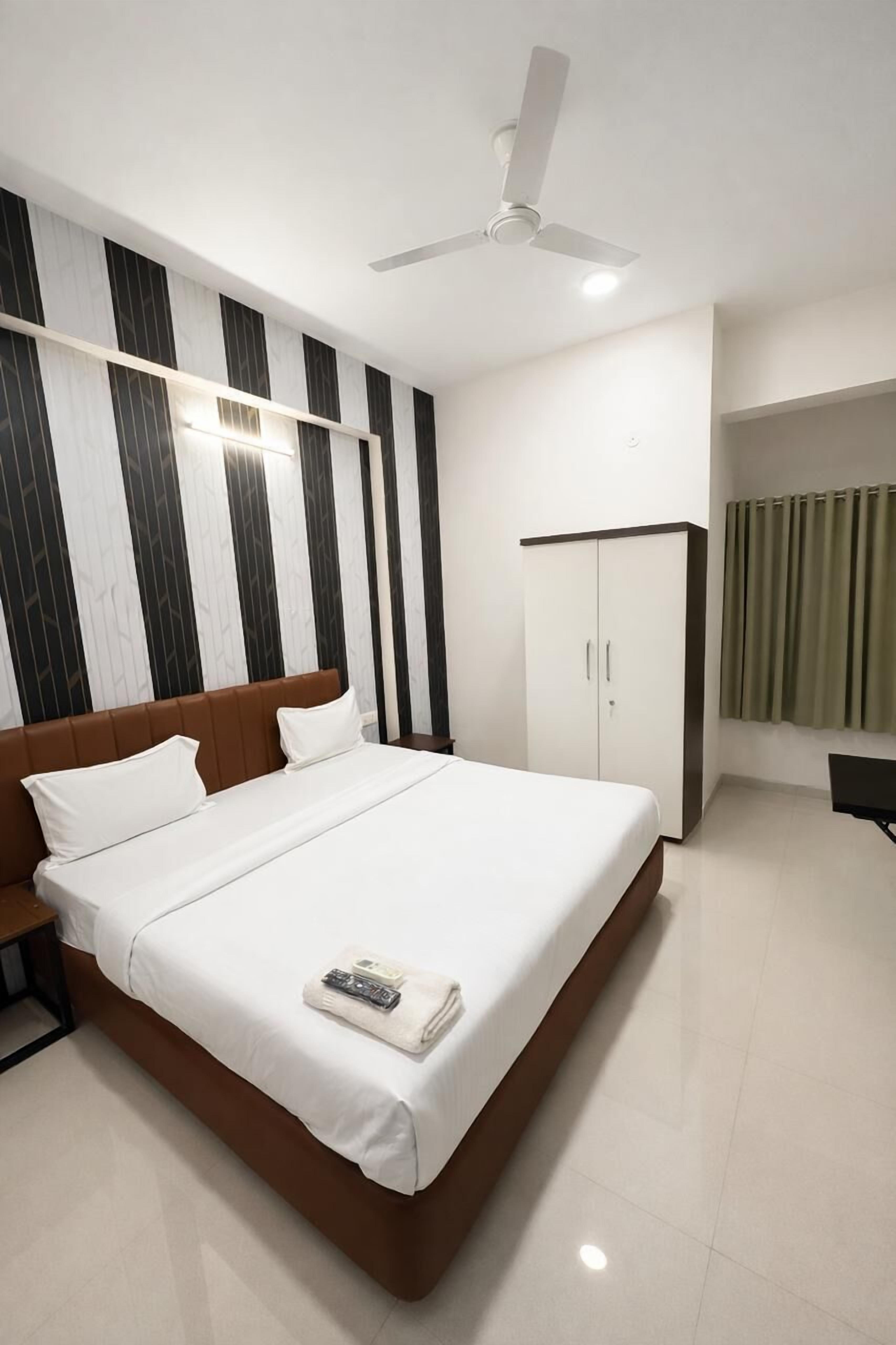 A modern hotel room with a large bed, a wardrobe, and a ceiling fan.