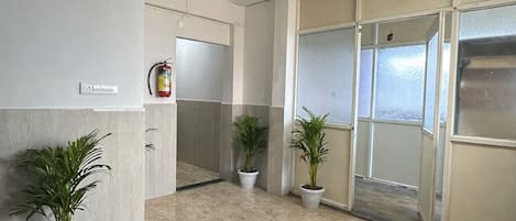 Un hall d’entrée spacieux, doté d’un sol carrelé, de plantes en pot, d’un extincteur et d’une porte donnant accès à une pièce.