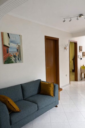 Un salon avec un canapé bleu, une porte en bois et un tableau accroché au mur.