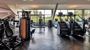 Une salle de sport moderne équipée de divers appareils d’exercice, dotée de grandes fenêtres et d’un plancher en bois.