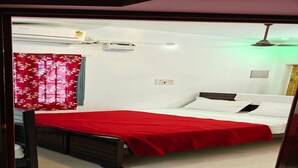 Une chambre à coucher avec un lit, une couvre-lit rouge, une fenêtre avec un rideau rouge, un climatiseur et un ventilateur de plafond.