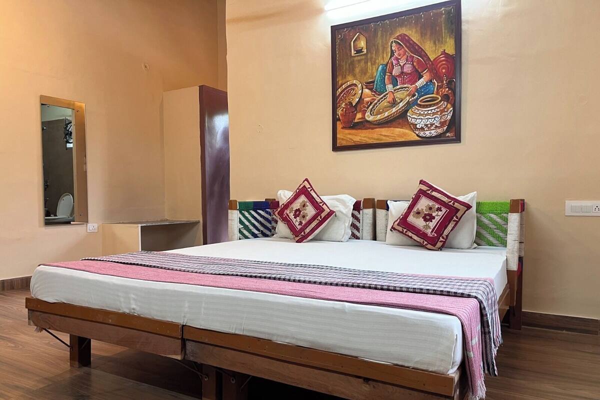 A neatly made bed with a wooden frame, a mirror on the wall, and a painting depicting a traditional scene.
