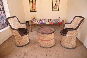 Une pièce avec deux fauteuils en osier, une petite table ronde et une couverture colorée posée sur un banc.