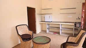 Ein kleines Zimmer mit zwei Korbstühlen, einem kleinen runden Tisch, einem Kühlschrank und einem Regal.