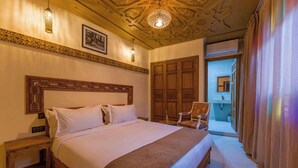 A bedroom with a large bed, wooden headboard, and a ceiling with intricate patterns. There is a chair and a small table beside the bed. - Riad Brothers (Marrakech)