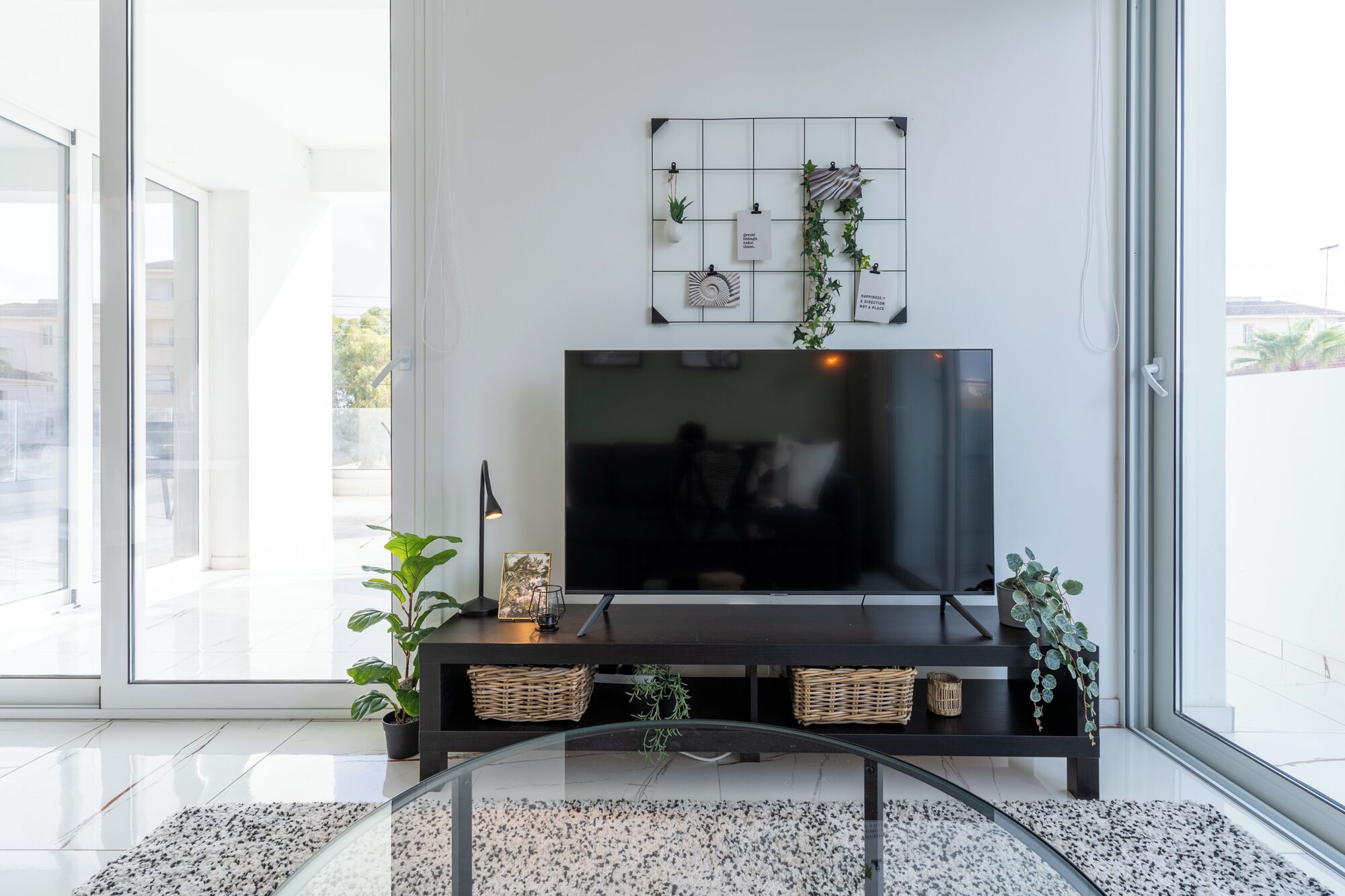 A modern living room with a large flat-screen TV, a black entertainment unit, and a glass coffee table.