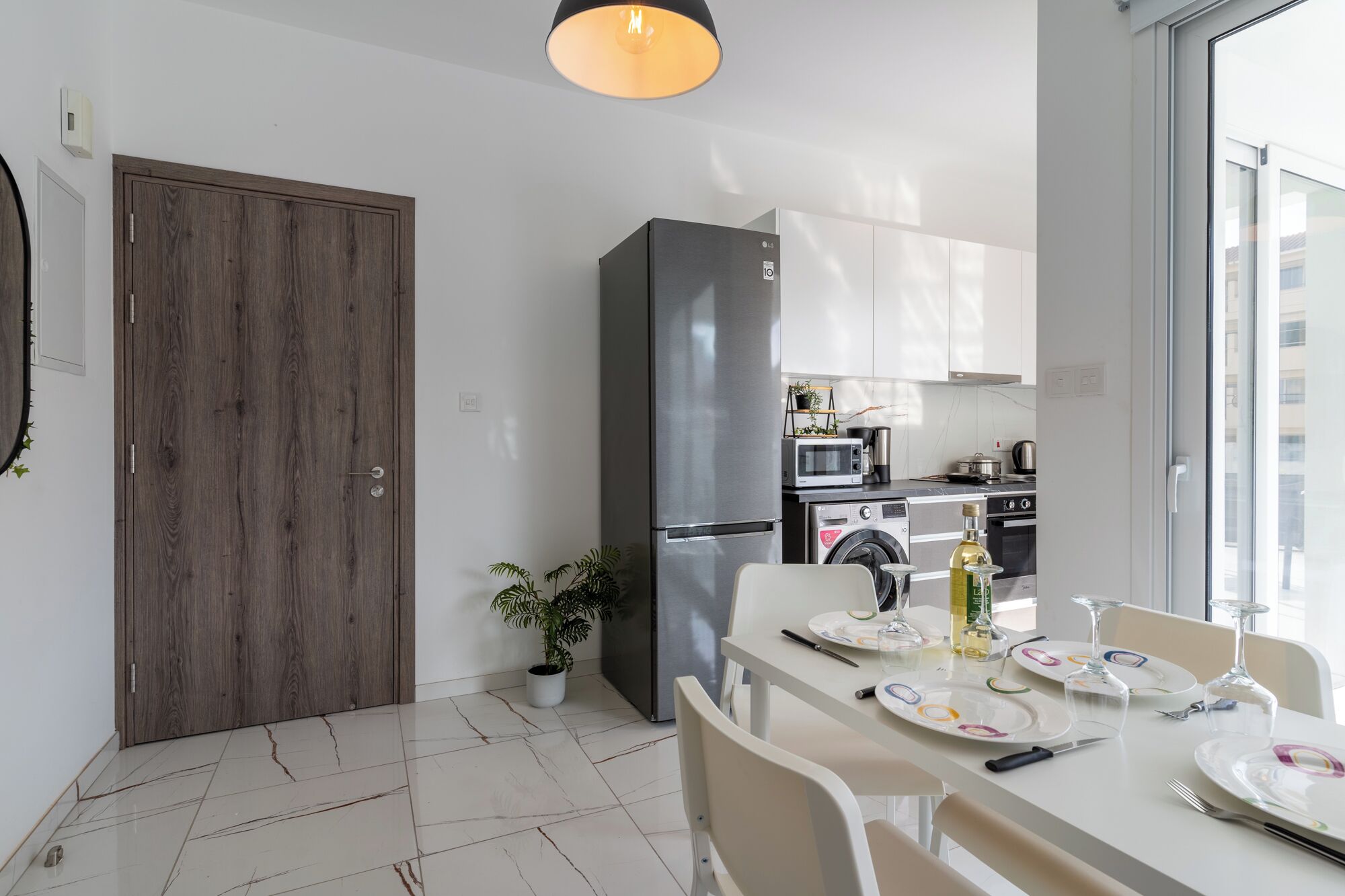 Una cocina moderna con refrigerador, microondas, horno y pileta. Hay una mesa de comedor con platos y una botella de aceite de oliva.